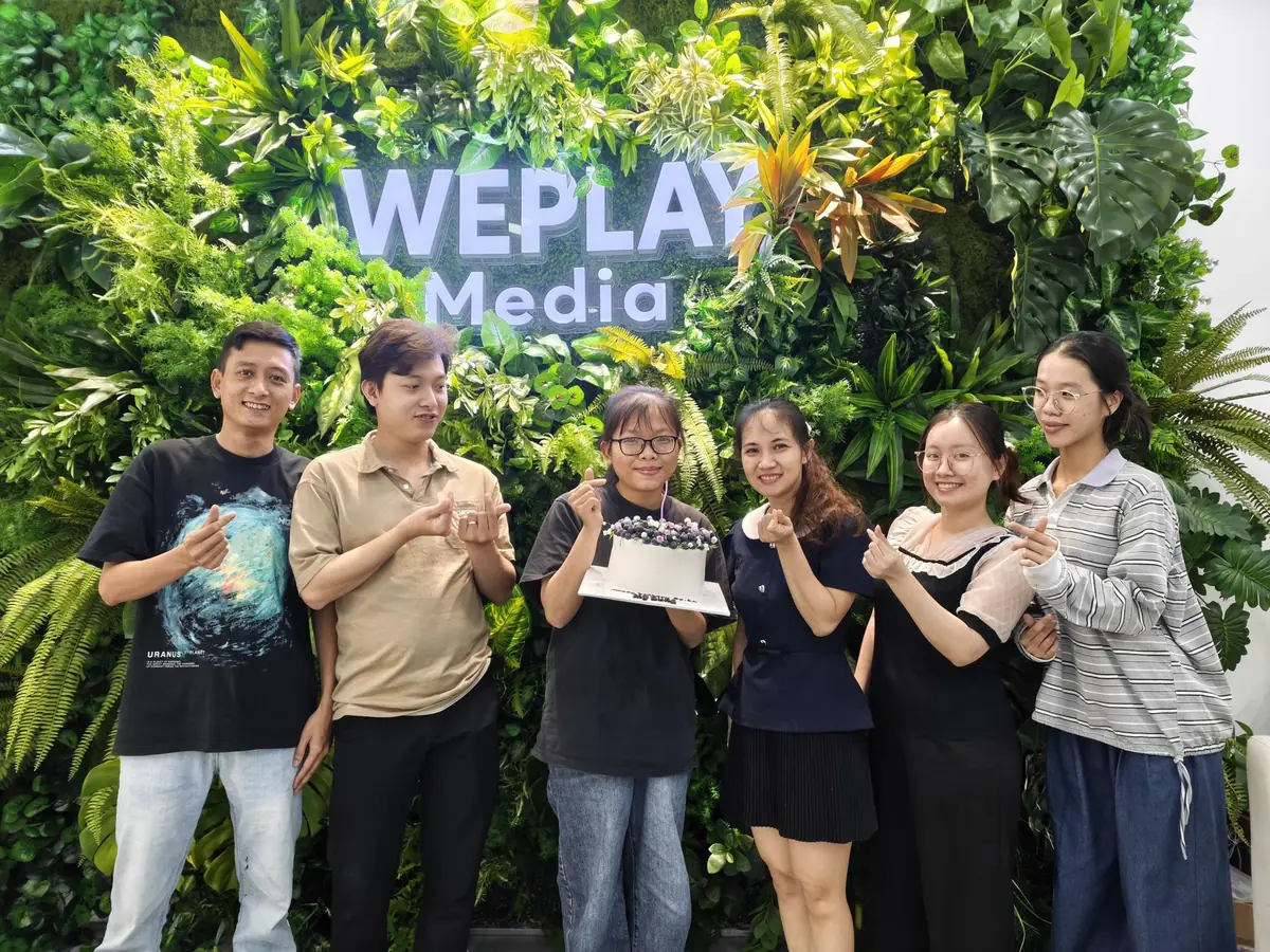 Đội ngũ Weplay Media trước bức tường logo văn phòng
